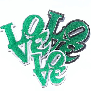 May include: Green and black felt patches spelling out the word "LOVE" in a stylized font. The patches are layered on top of each other.