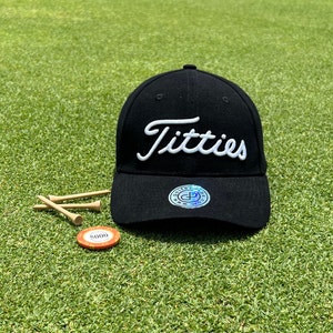 May include: Black baseball cap with a white embroidered "Titties" logo. The cap has a black adjustable strap and a small black and white logo on the back.