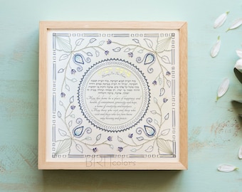 Puede incluir: Un lienzo blanco enmarcado con un diseño bordado en azul y blanco. El diseño presenta un círculo con texto en hebreo y una bendición para el hogar. El texto dice: "Que este hogar sea un lugar de felicidad y salud, de satisfacción, generosidad y esperanza. Un hogar de creatividad y amabilidad. Que quienes lo visiten y quienes lo visiten y quienes vivan aquí conozcan solo bendiciones y paz."