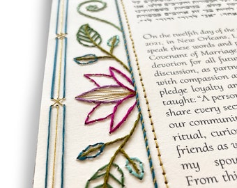May include: A close-up of a wedding ketubah with a floral design embroidered in green, blue, and purple thread. The text on the ketubah is in Hebrew and English. The English text reads: "On the twelfth day of the 2021, in New Orleans, LA, we speak these words and Covenant of Marriage devotion for all future discussion, as partners with compassion and pledge loyalty and taught: "A person share every second of our community ritual, curious friends as we my spouse From this"