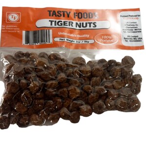 May include: A clear plastic bag filled with brown tiger nuts. The bag has a label that reads "Tasty Foods Tiger Nuts" and "Unbeatable Quality". The label also states that the nuts are 100% natural and have a net weight of 3 oz / 56g.