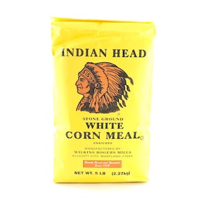 May include: A yellow bag of Indian Head Stone Ground White Corn Meal. The bag features a black and red illustration of an indigenous person wearing a headdress. The text "Indian Head Stone Ground White Corn Meal" is printed in black. The bag is 5 pounds (2.27 kg).