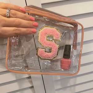 Puede incluir: Bolsa transparente de plástico con cremallera con una letra 'S' de peluche rosa y una botella de esmalte de uñas rosa en su interior.