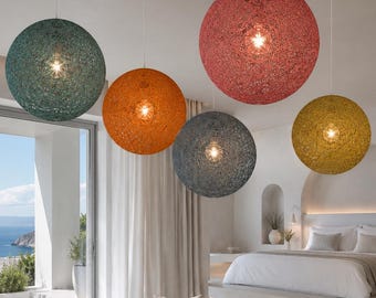Może przedstawiać: Nowoczesny salon z pięcioma kulistymi lampami wiszącymi w odcieniach zieleni, pomarańczy, czerwieni, szarości i żółci. Lampy zwisają z sufitu, oświetlając pokój w neutralnych tonacjach z sofą, krzesłem i łóżkiem.