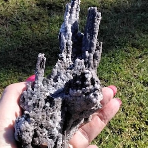 May include: A gray and white crystal formation with a rough, textured surface. The crystal is shaped like a cluster of spires.