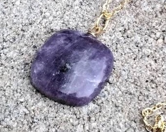 May include: A gold chain necklace with a large, flat, purple gemstone pendant. The pendant has a slightly irregular shape and a cloudy, translucent appearance.