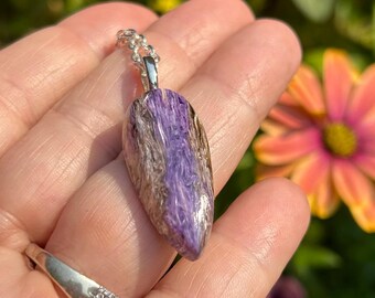 May include: A silver chain necklace with a purple and silver pendant. The pendant is a teardrop shape and has a shimmery, iridescent finish.