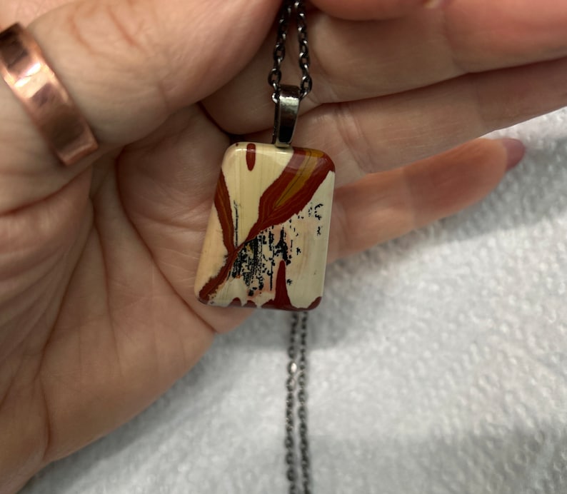 May include: A silver chain necklace with a rectangular pendant made of a colorful, patterned stone. The stone has shades of red, white, and black.
