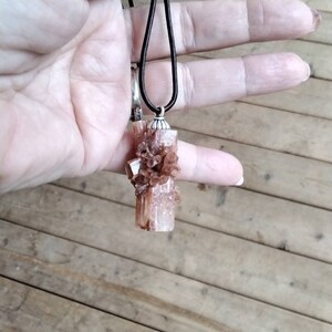 May include: A brown and white crystal pendant on a black cord necklace. The crystal is a cluster of small crystals with a larger crystal in the center.