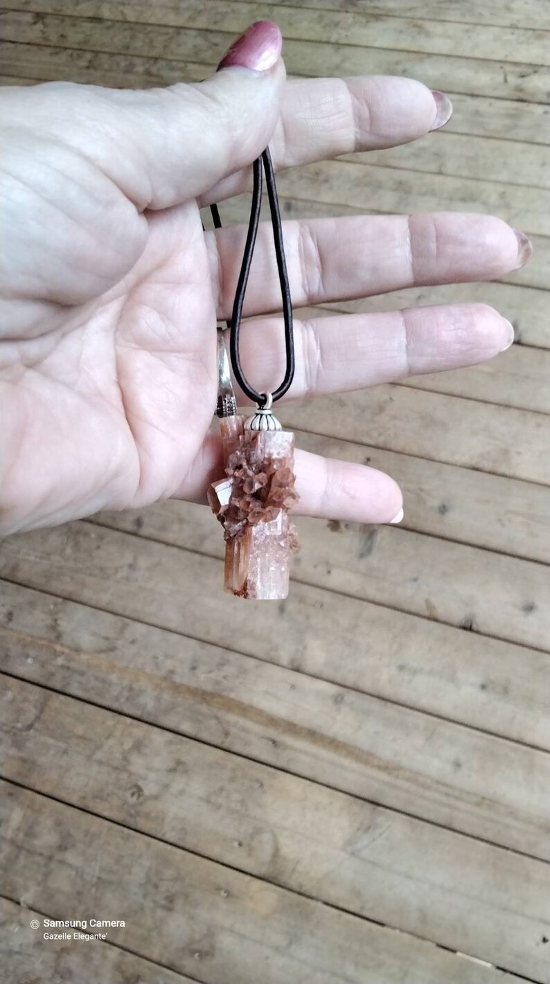 May include: A brown and white crystal pendant on a black cord necklace. The crystal is a cluster of small crystals with a larger crystal in the center.