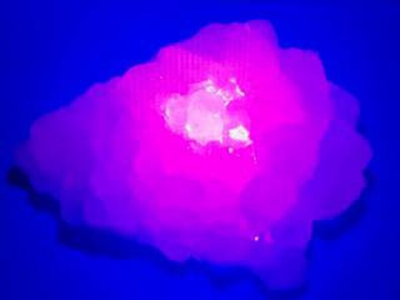 May include: A large, white, crystalline rock with a pink glow under a black light. The rock has a rough, textured surface and a large, flat, white area in the center.