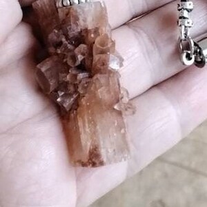 May include: A brown crystal pendant with a silver clasp on a brown leather cord necklace.