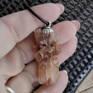 May include: A brown crystal pendant with a silver bail. The crystal is a cluster of small crystals that are translucent and have a slight orange hue.