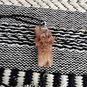 May include: A brown crystal pendant with a silver bail, hanging from a brown leather cord. The crystal is a cluster of small, pointed crystals.