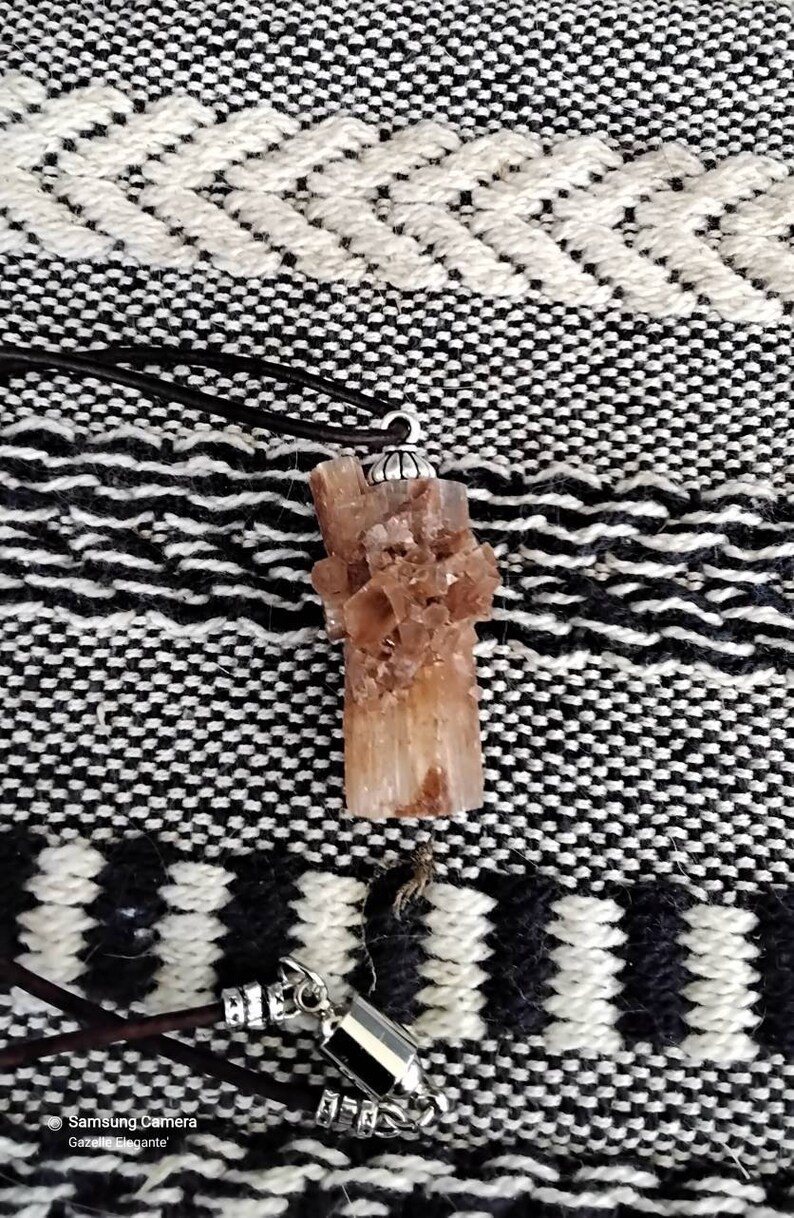 May include: A brown crystal pendant with a silver bail, hanging from a brown leather cord. The crystal is a cluster of small, pointed crystals.