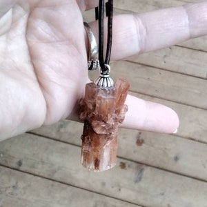 May include: A brown leather cord necklace with a brown crystal pendant. The crystal is a cluster of small crystals.