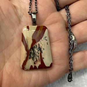 May include: A silver chain necklace with a rectangular pendant featuring a colorful, abstract pattern in shades of brown, red, and white.