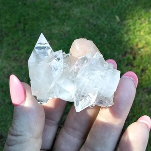 May include: A cluster of clear quartz crystals with a pink calcite crystal in the center. The crystals are arranged in a pyramid shape.