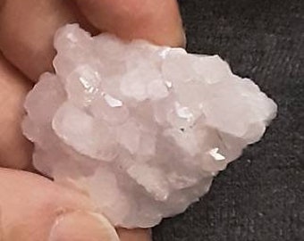 May include: A cluster of small, pale pink crystals. The crystals are clustered together in a rough, natural formation.