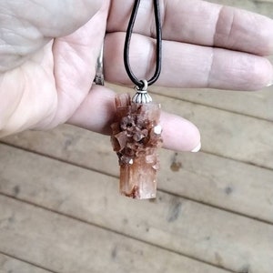 May include: A brown and white crystal pendant on a brown leather cord. The crystal is a cluster of small, pointed crystals.