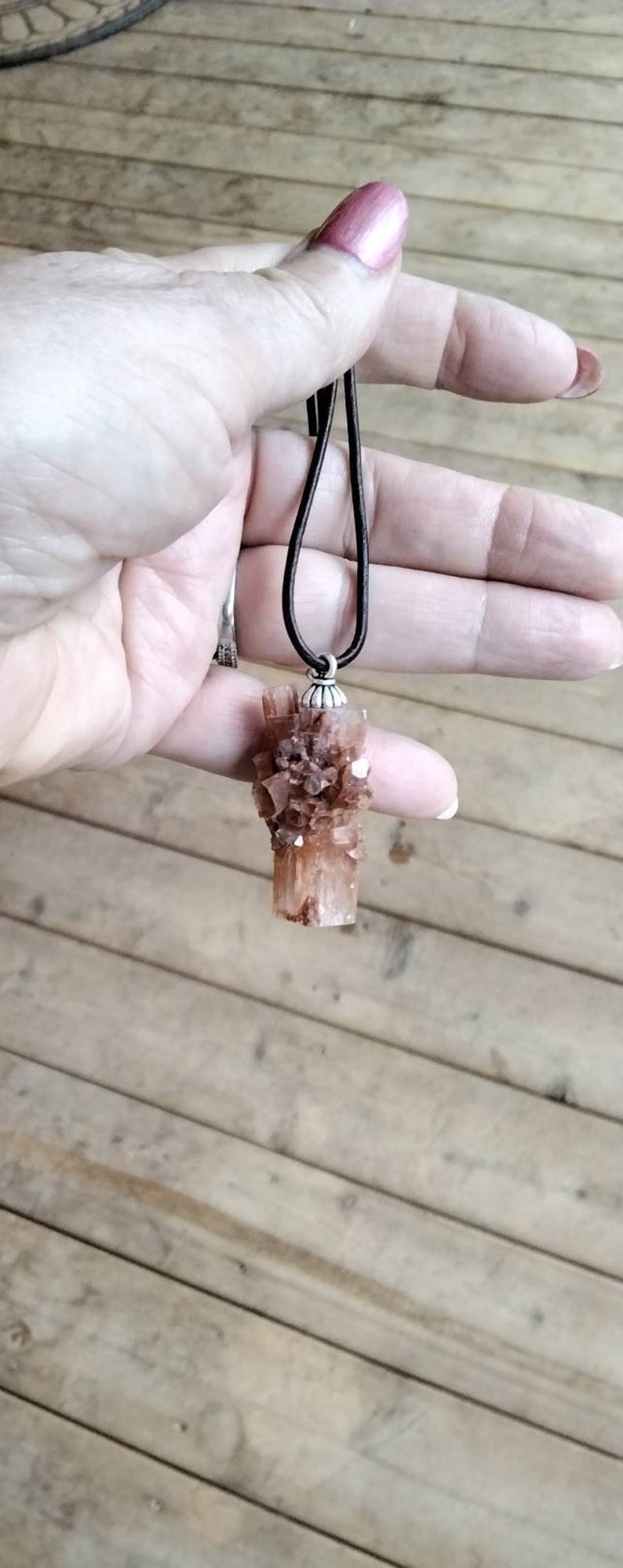 May include: A brown and white crystal pendant on a brown leather cord. The crystal is a cluster of small, pointed crystals.