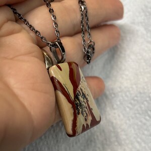 May include: A silver chain necklace with a rectangular pendant made of brown, white, and red jasper.