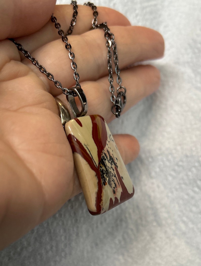 May include: A silver chain necklace with a rectangular pendant made of brown, white, and red jasper.