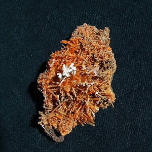 May include: A cluster of orange and white crystals on a dark background. The crystals are arranged in a random pattern and have a rough, textured surface.