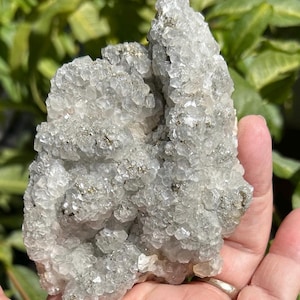 May include: A cluster of translucent, crystalline mineral formations featuring a jagged, irregular surface texture. The specimen displays a pale, icy white coloration with small, metallic gold-toned inclusions embedded throughout the structure.