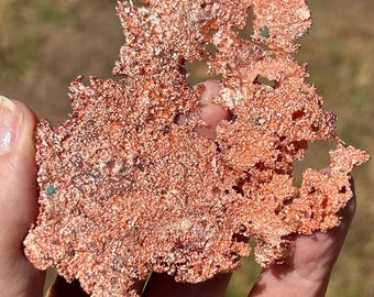 May include: A raw, metallic copper specimen with a highly textured, crystalline surface. The piece features an irregular, branching shape with a bright, reddish-orange luster and small, scattered green mineral inclusions throughout the structure.