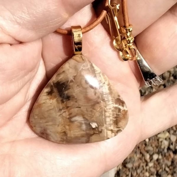May include: A brown and gold pendant necklace with a large, triangular, brown and white agate stone. The necklace is on a brown leather cord.