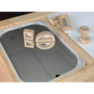 May include: A wooden play table featuring a mirror inset and various wooden shapes, including a circle, a square, and a rectangle. The shapes are all crafted from natural wood and have a smooth finish.