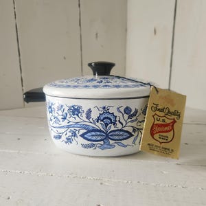 May include: White and blue enamelware cooking pot with a black handle and lid. The pot features a floral design in shades of blue. A vintage tag reads "Finest Quality U.S. Gourmet Cook Ware".