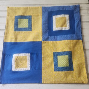May include: A blue and yellow patchwork quilt with a square pattern. The quilt is made of different fabrics with various patterns, including polka dots, swirls, and small floral prints.