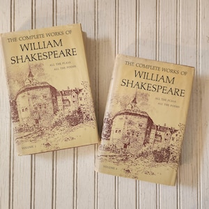 May include: Two vintage books titled "The Complete Works of William Shakespeare." The covers are beige with a sepia-toned illustration of a building and text. Volume 1 and Volume 2 are visible.