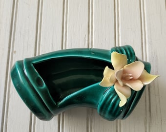 May include: A green ceramic planter shaped like a curved, tied ribbon with a pink and yellow flower on top.