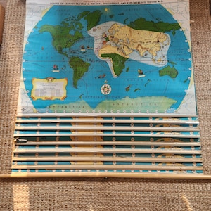 May include: A vintage wall-mounted pull-down map titled The Tryon Illustrated American History Maps: Routes of Certain Travelers, Traders, Discoverers, and Explorers, 1270 to 1700 A.D. The map features a world view with blue oceans and green land.