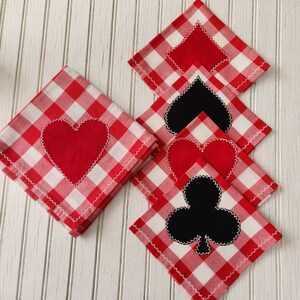 May include: Set of four red and white gingham fabric napkins with embroidered playing card symbols. The symbols include a heart, spade, club, and diamond.