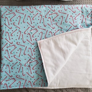 May include: A blue and white quilt with a candy cane pattern on one side and a plain white side on the other. The quilt is folded in half, showing both sides.