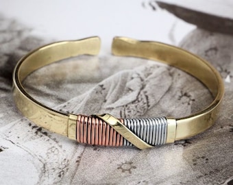 Könnte beinhalten: Ein goldfarbenes Armreif-Armband mit einem gedrehten Design aus Kupfer und Silber.