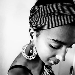 May include: A black and white photograph of a person wearing a black and white striped headband and large silver hoop earrings. The person is looking down.