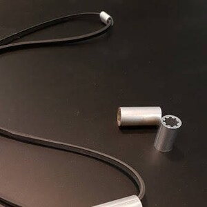 May include: Two silver metal cord ends with a black leather cord. One cord end has a star-shaped pattern.