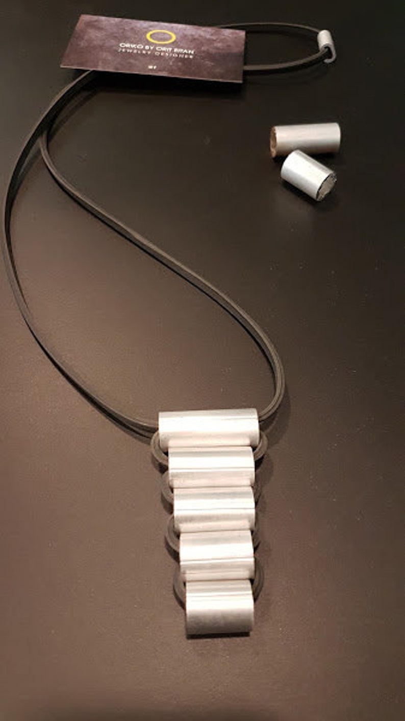 May include: A silver necklace with a layered pendant made of stacked silver rings. The necklace is on a black cord.