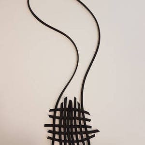 May include: A black leather necklace with a woven pendant. The pendant is made of thin strips of leather that are woven together to create a geometric pattern.