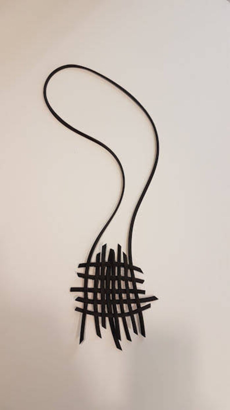 May include: A black leather necklace with a woven pendant. The pendant is made of thin strips of leather that are woven together to create a geometric pattern.