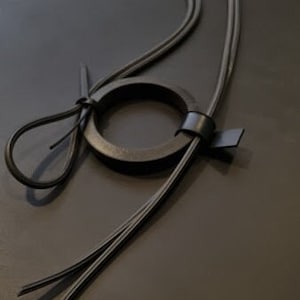 May include: A black leather necklace with a circular pendant. The necklace is made of two strands of leather that are tied together at the top. The pendant is a simple circle of leather.