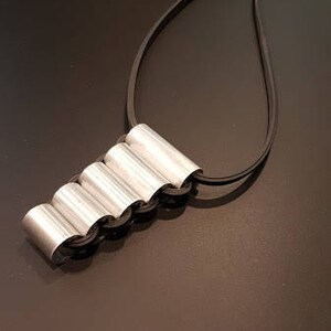 May include: A silver necklace with a unique pendant made of five connected cylindrical shapes. The pendant is attached to a black cord.