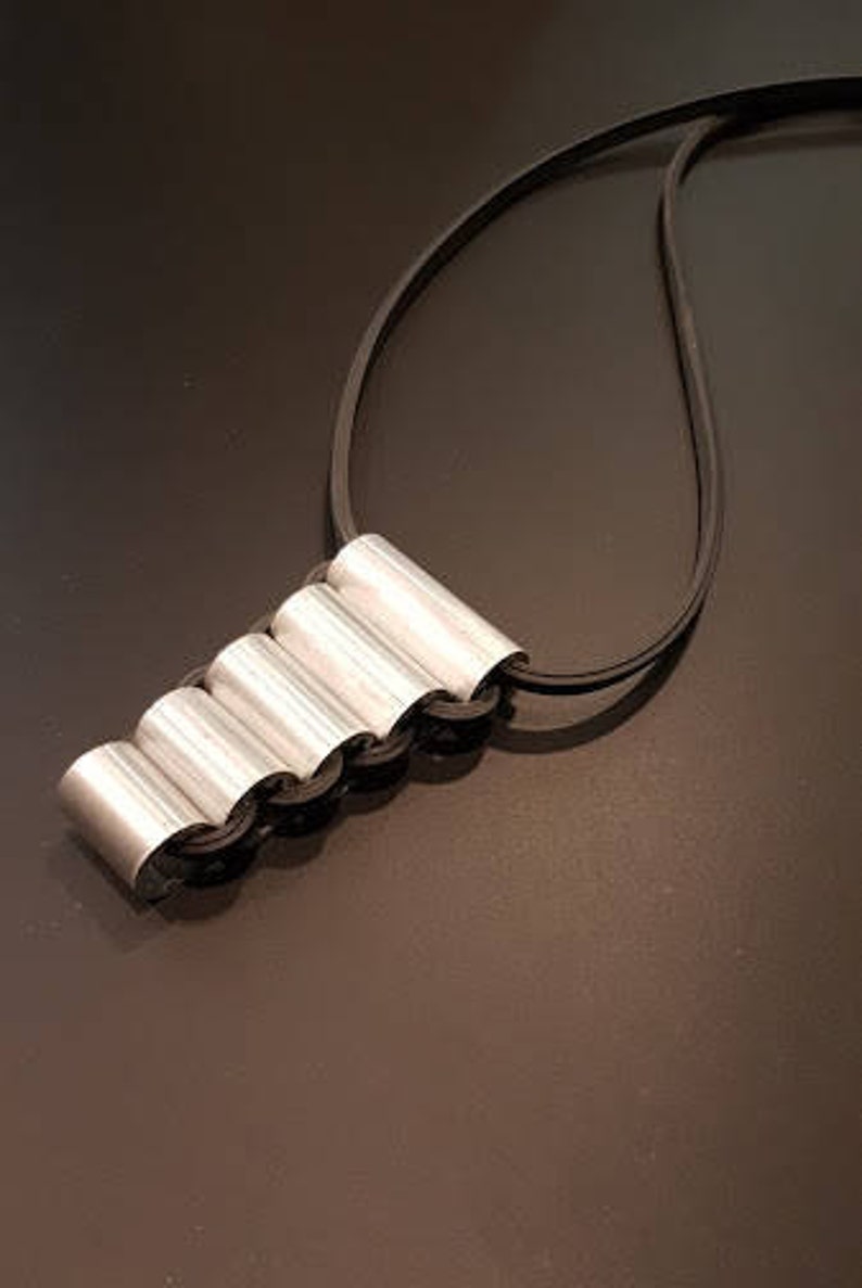 May include: A silver necklace with a unique pendant made of five connected cylindrical shapes. The pendant is attached to a black cord.