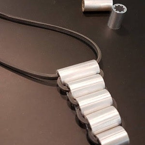 May include: A silver necklace with a chain made of multiple connected cylinders. The necklace is on a black surface.