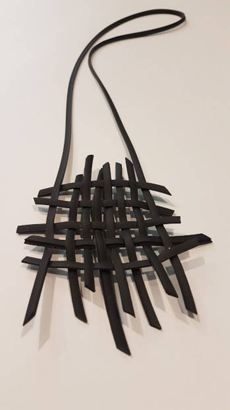 May include: A black woven necklace with a long, thin chain. The necklace is made of multiple strands of black material that are woven together to create a lattice pattern.